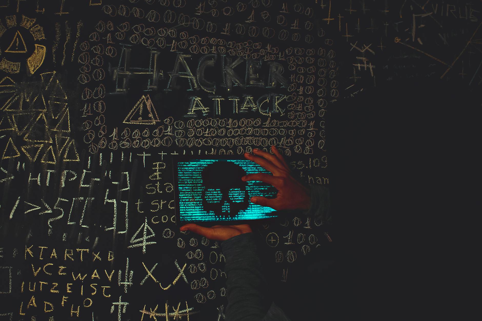 Haker w czarnej bluzie patrzy na tablet z czaszką i napisem Hacker Attack