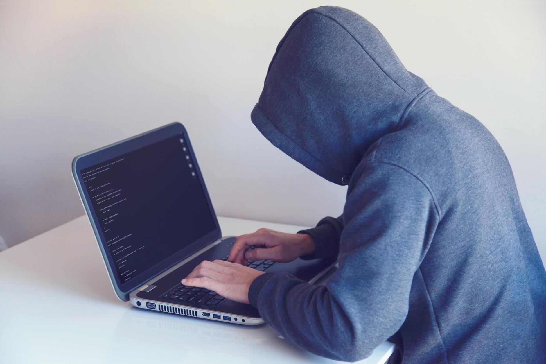 Haker w kapturze pracujący przy laptopie przy białym biurku