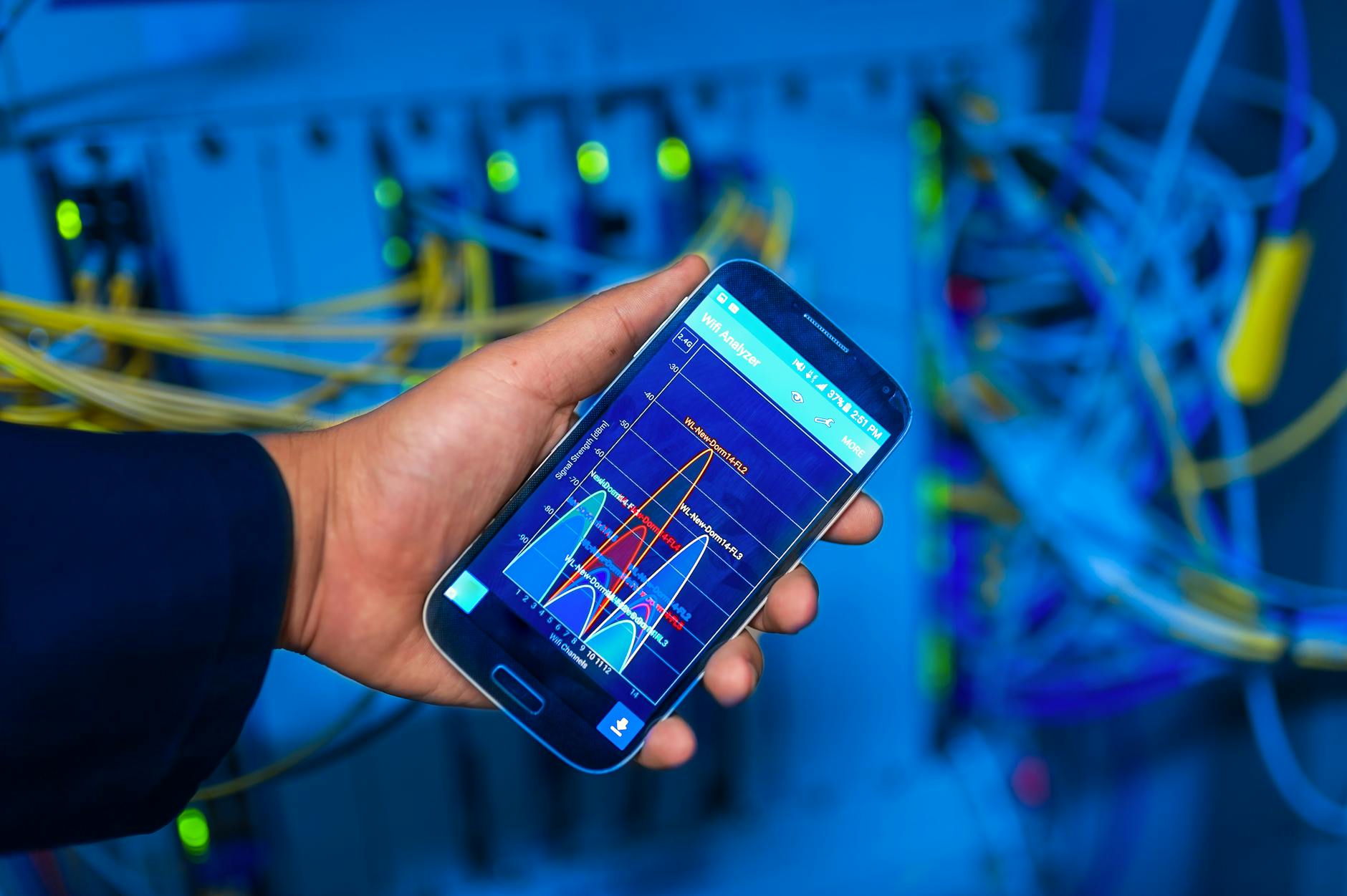 Dłoń trzymająca smartfon z analizą sieci na tle serwerowni
