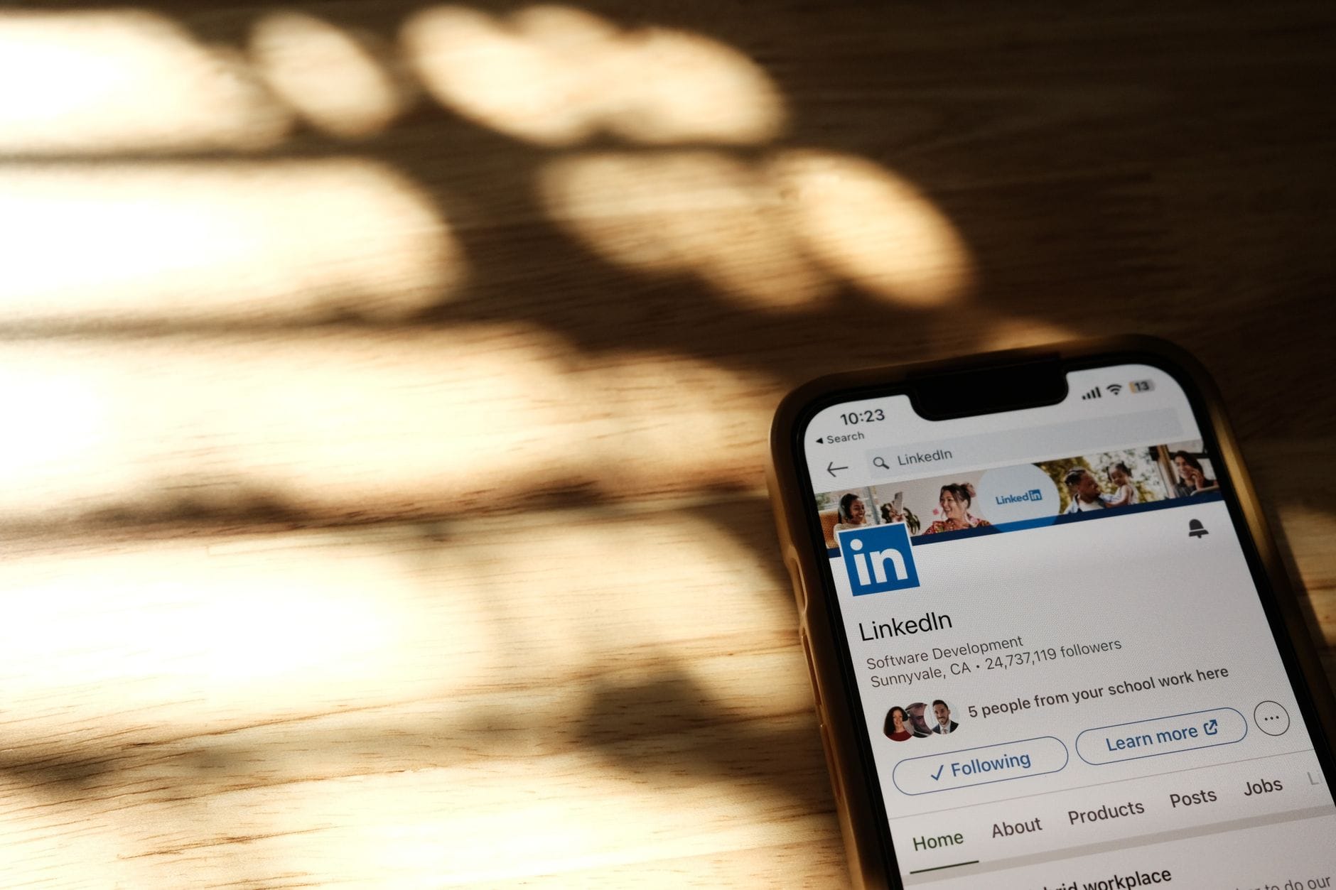Smartfon z profilem LinkedIn specjalisty IT leżący na drewnianym stole